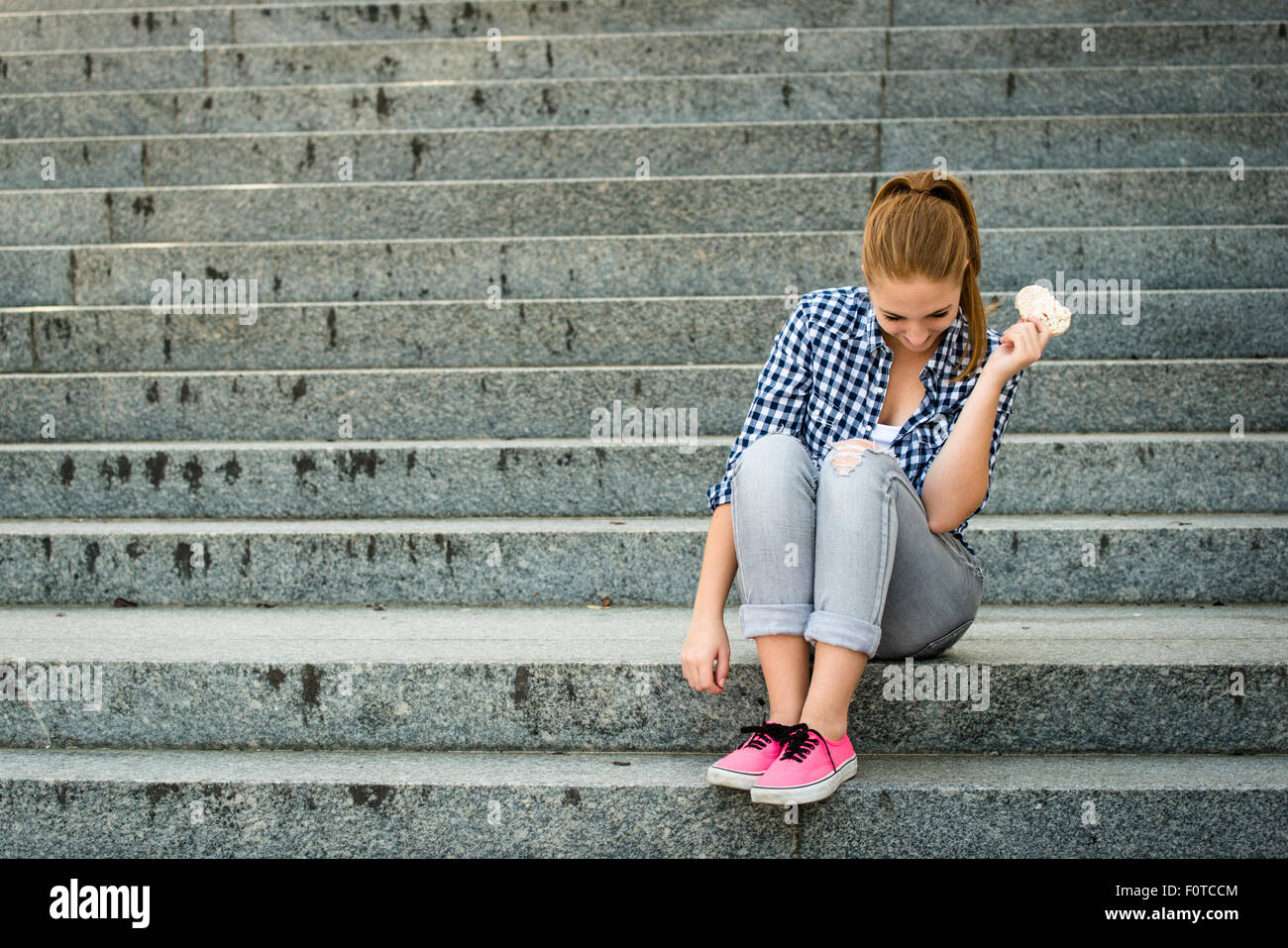 Mode de vie sain - manger du pain soufflé adolescent assis sur des escaliers extérieurs Banque D'Images