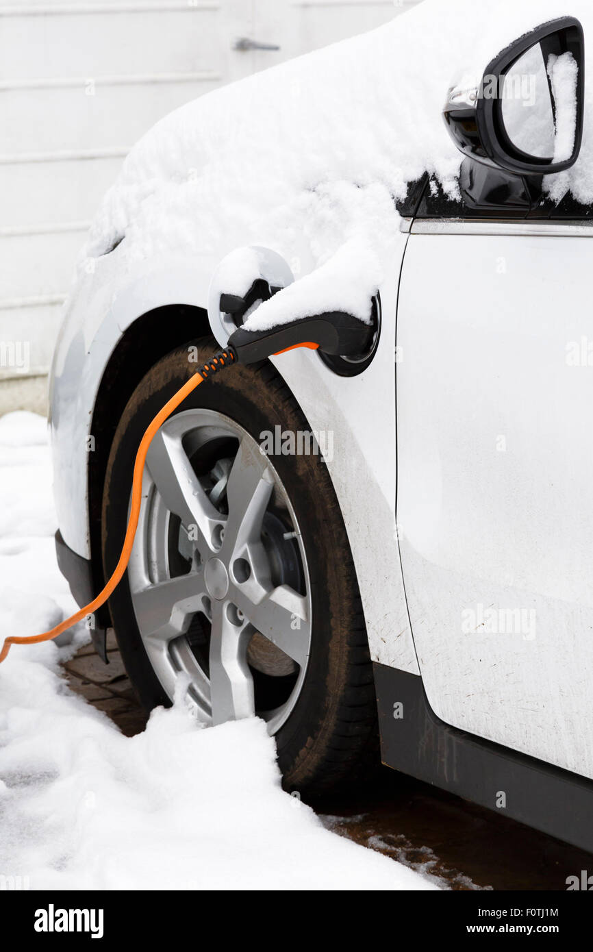 Voiture électrique branché à une prise secteur de recharger à l'extérieur dans la neige d'hiver Banque D'Images