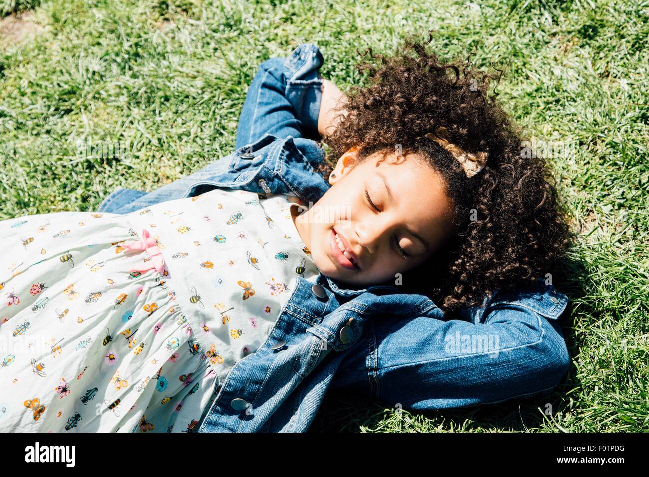 High angle view of girl allongé sur le dos sur l'herbe, les mains derrière la tête, les yeux fermés Banque D'Images