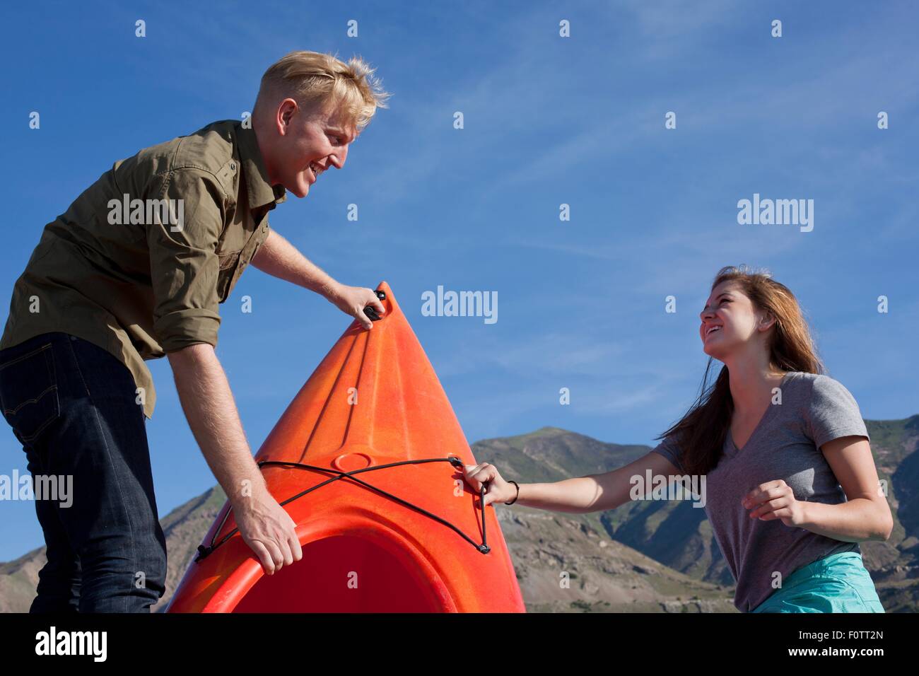 Young couple preparing kayak orange, se regardant en souriant Banque D'Images Young couple preparing kayak orange, se regardant en souriant Banque D'Images
