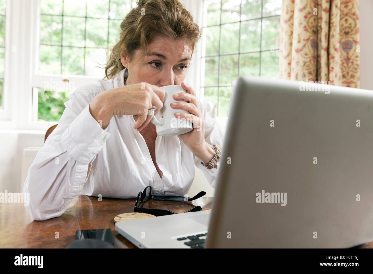 Inquiets mature woman working on laptop tout en buvant du café dans la salle de séjour Banque D'Images