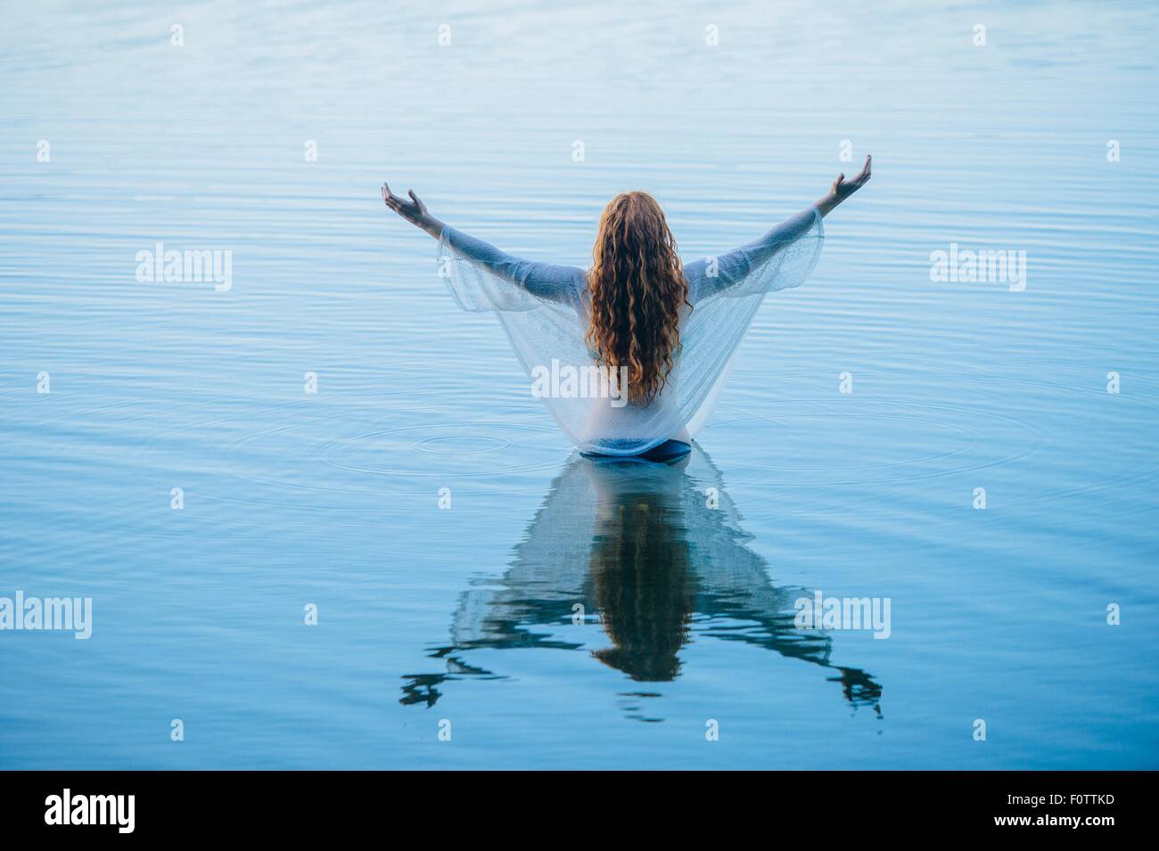 Young woman standing in blue lake avec les bras ouverts Banque D'Images