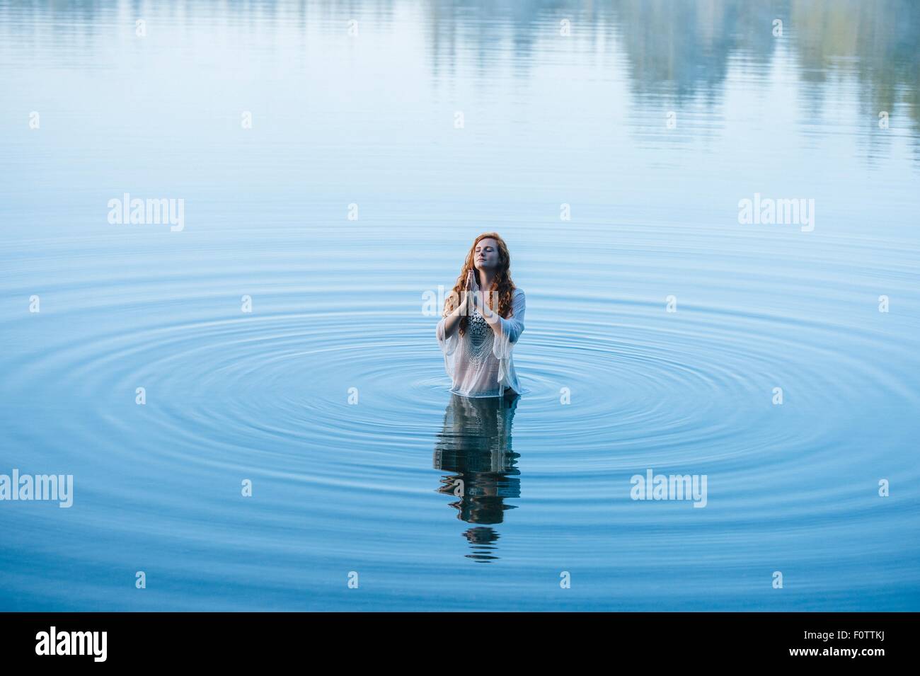 Jeune femme debout dans le lac ripples prier avec les yeux fermés Banque D'Images