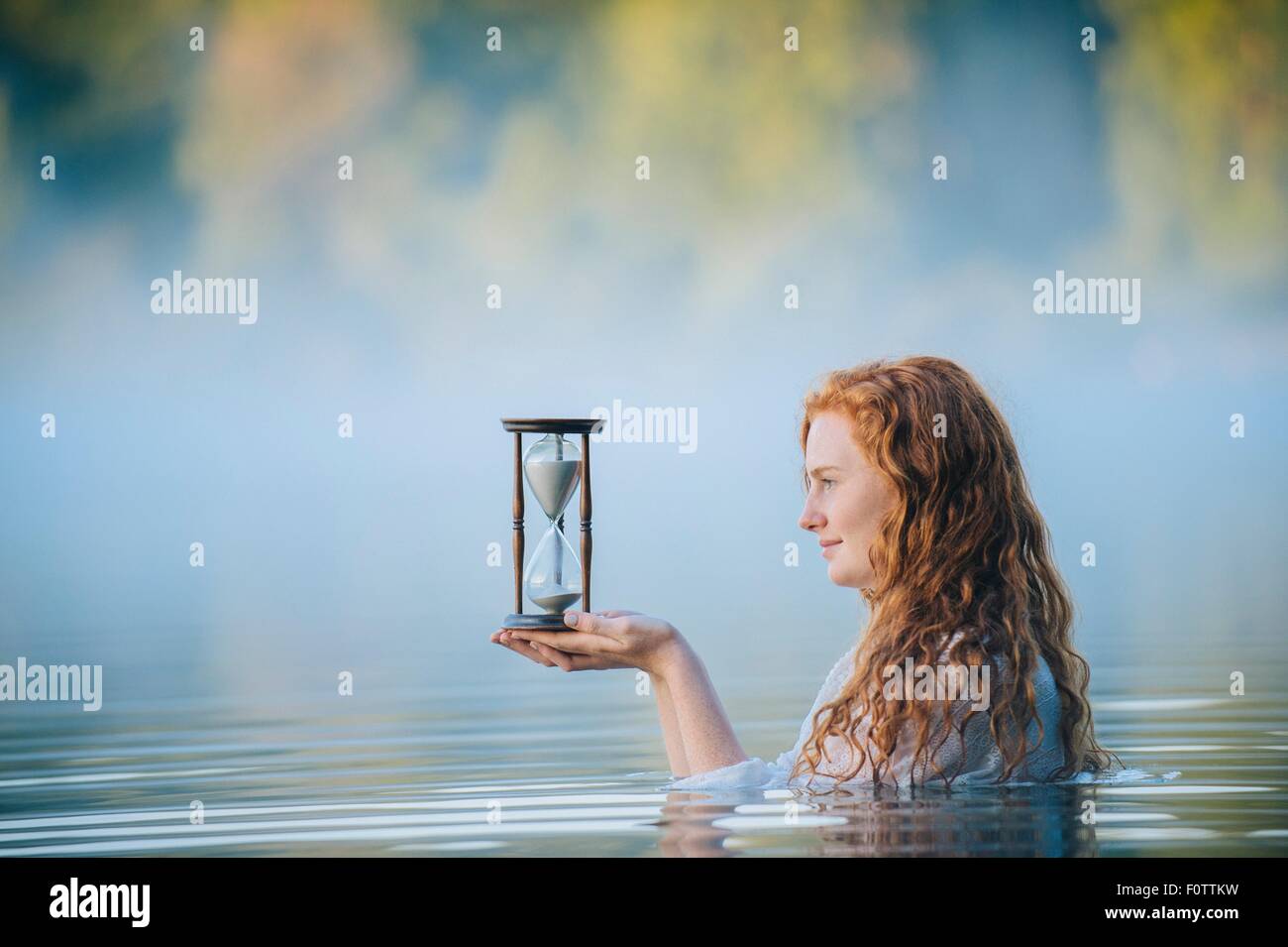 Jeune femme debout dans le lac Misty contemplant hourglass Banque D'Images