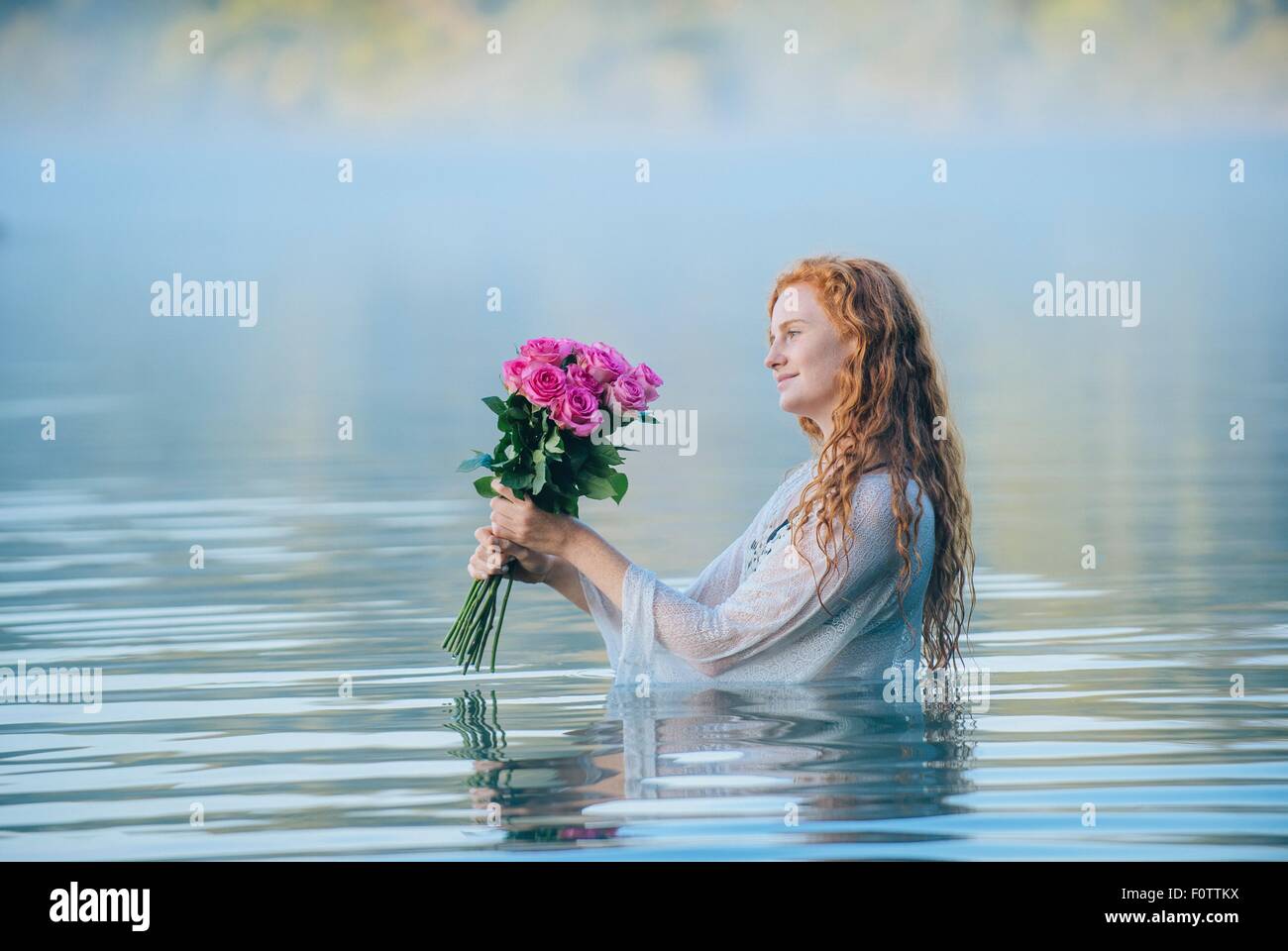 Jeune femme debout dans le lac en regardant bouquet de roses roses Banque D'Images