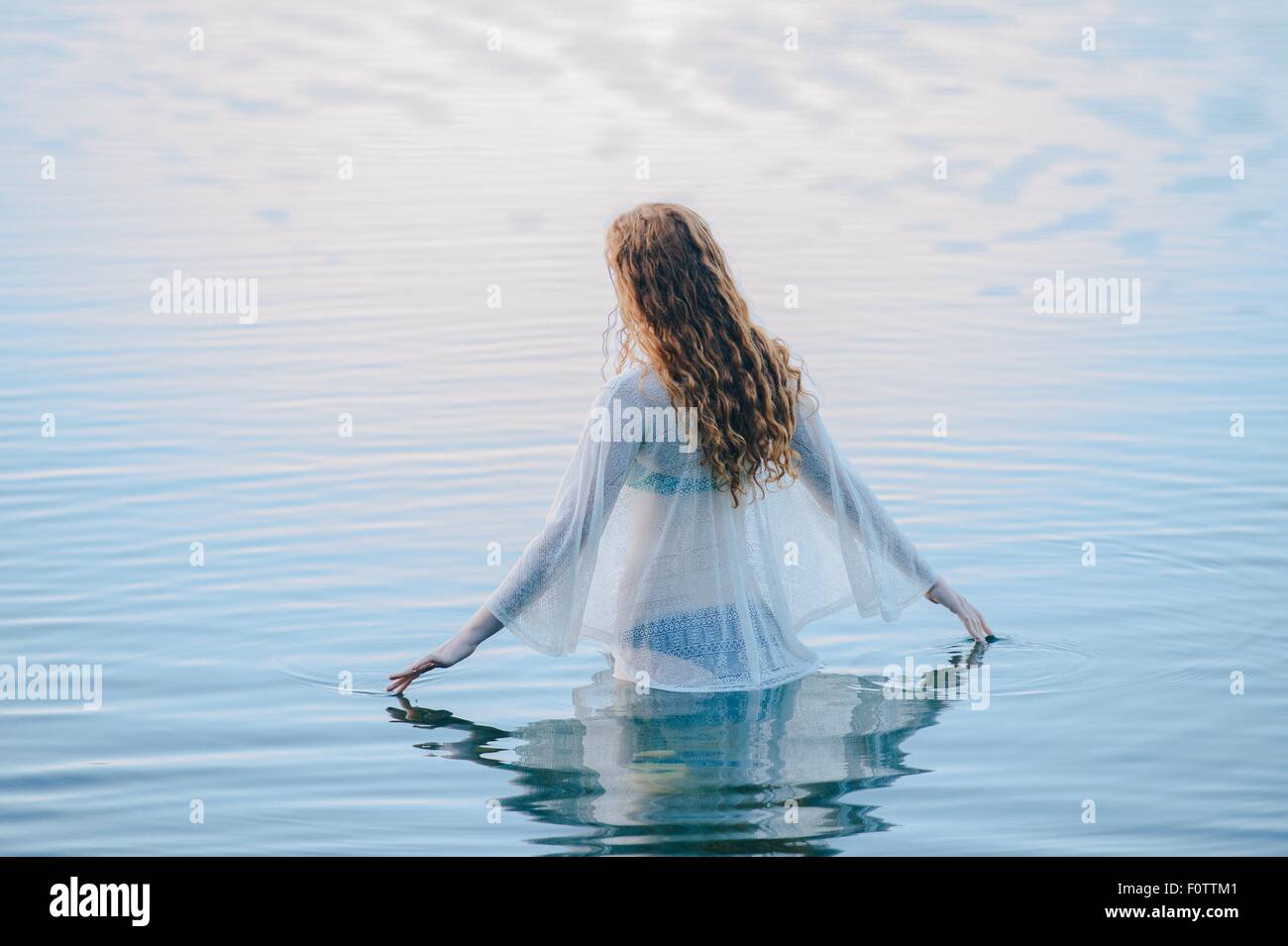 Vue arrière du young woman standing in lake surface ondulée avec ses doigts Banque D'Images