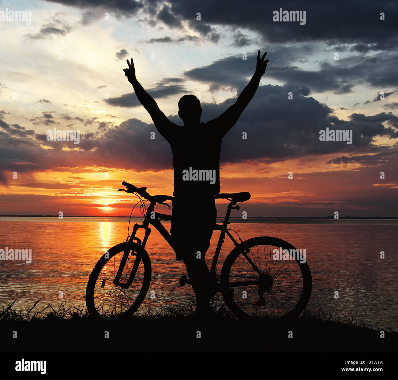 Silhouette d'un homme avec un vélo de montagne sur la rive du fleuve au coucher du soleil Banque D'Images