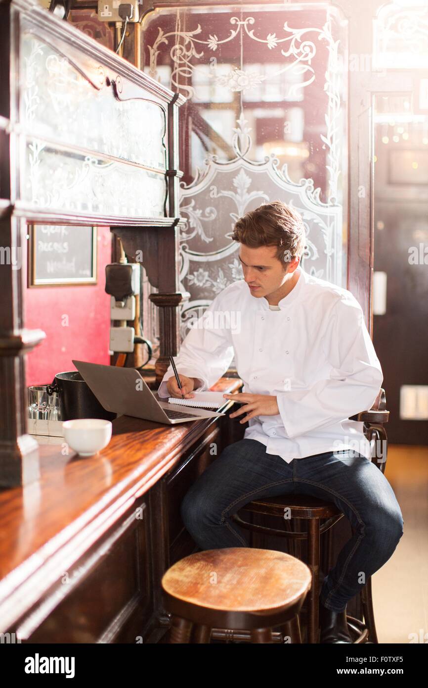 Jeune chef assis sur tabouret de bar au travail à l'aide d'ordinateur portable Banque D'Images