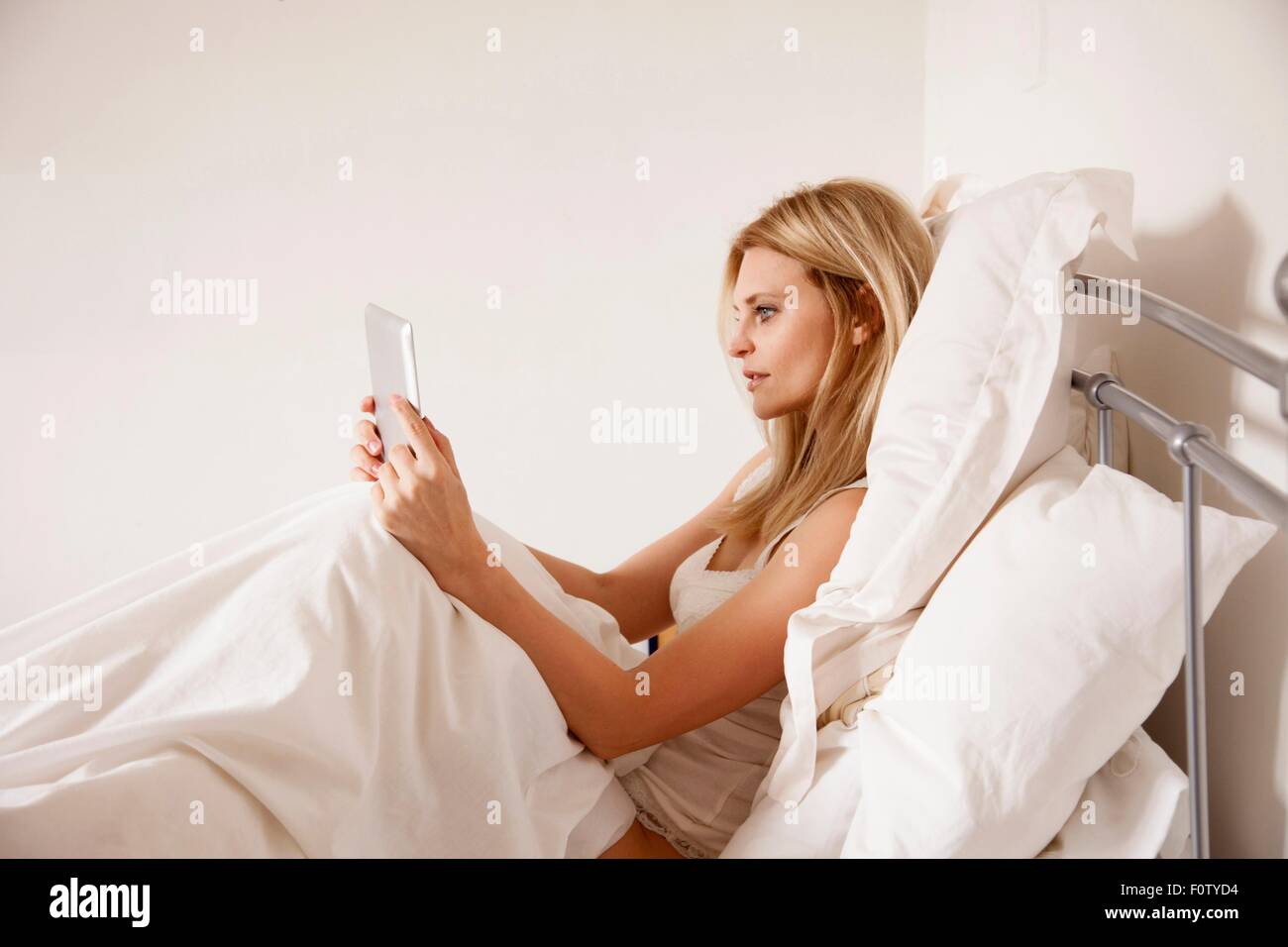 Mid adult woman sitting up in bed using digital tablet Banque D'Images