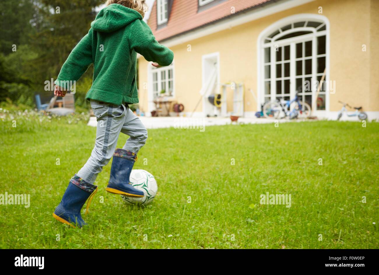 Vue arrière du boy wearing Wellington à jouer au football dans le jardin Banque D'Images
