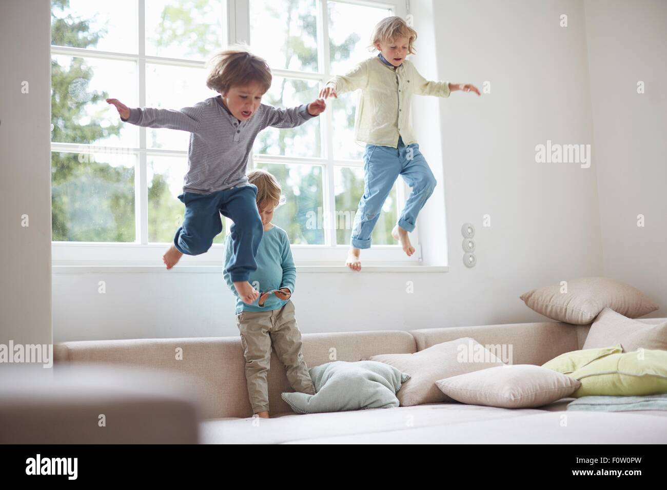 Trois garçons sautant hors de la fenêtre sur canapé, mid air Banque D'Images