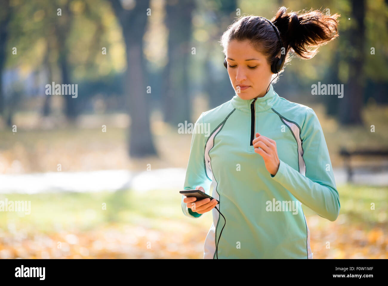 Jeune femme avec un casque jogging en automne nature et à la recherche de téléphone mobile Banque D'Images