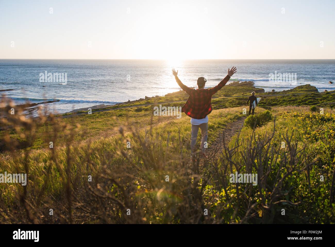 Jeune homme avec bras levés à la suite de surfeur sur coast path Banque D'Images
