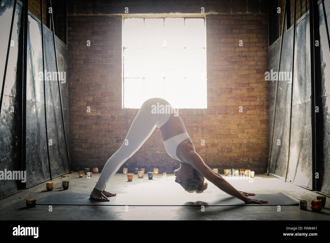 Une femme blonde, dans un blanc petit top et leggings, se pencher sur le sol entourée de bougies, dans une position de yoga. Banque D'Images