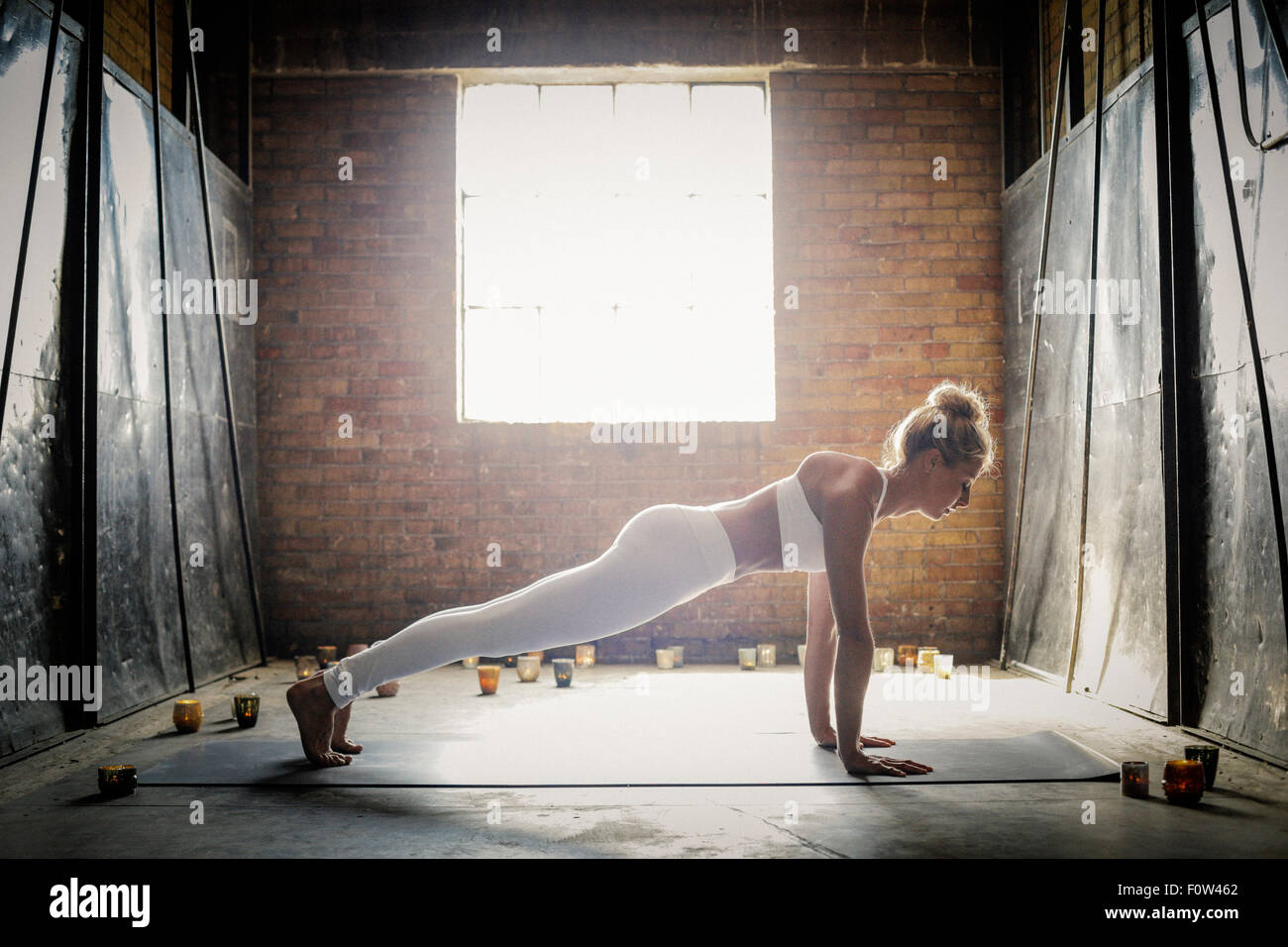 Une femme blonde, dans un blanc petit top et leggings, se pencher sur le sol entourée de bougies, faisant du yoga. Banque D'Images