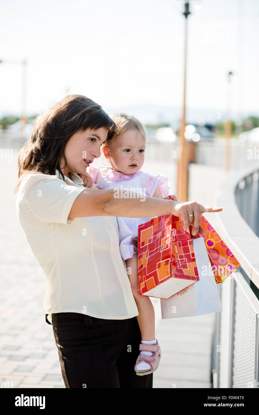 Maman avec petite fille en robe blanche holding shopping bags à quelque part Banque D'Images