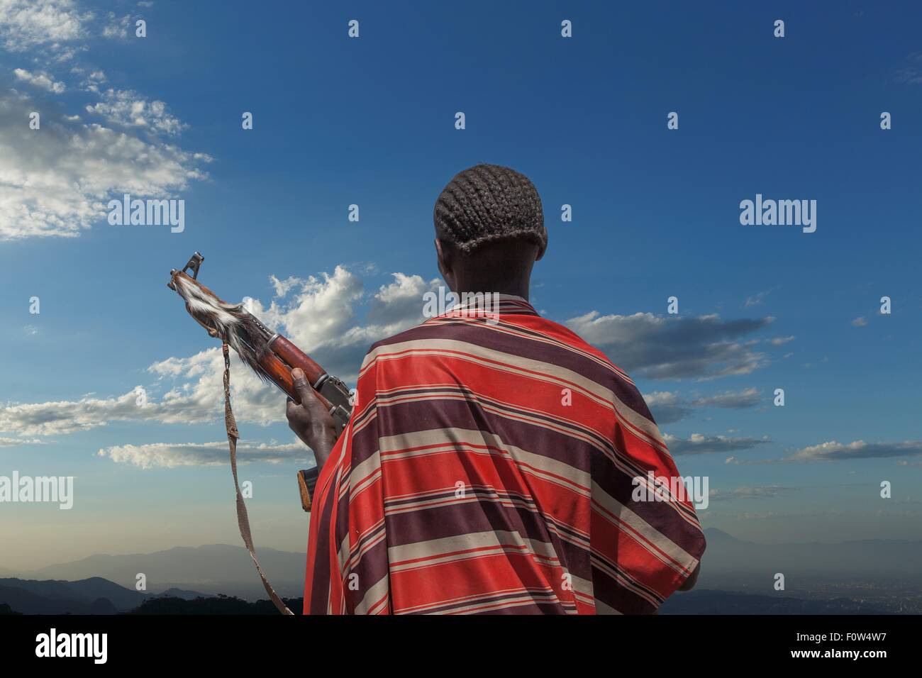 Vue arrière du jeune homme de la tribu Karo avec Kalachnikov, regardant son troupeau , Ethiopie, Afrique Banque D'Images