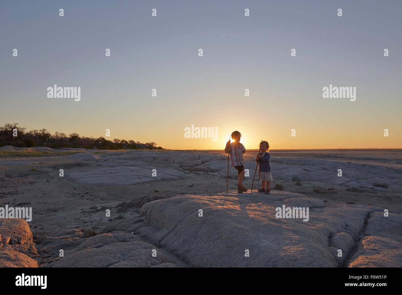 Deux garçons debout sur un rocher, tenant une lance, coucher de soleil, Gweta, makgadikgadi, Botswana Banque D'Images