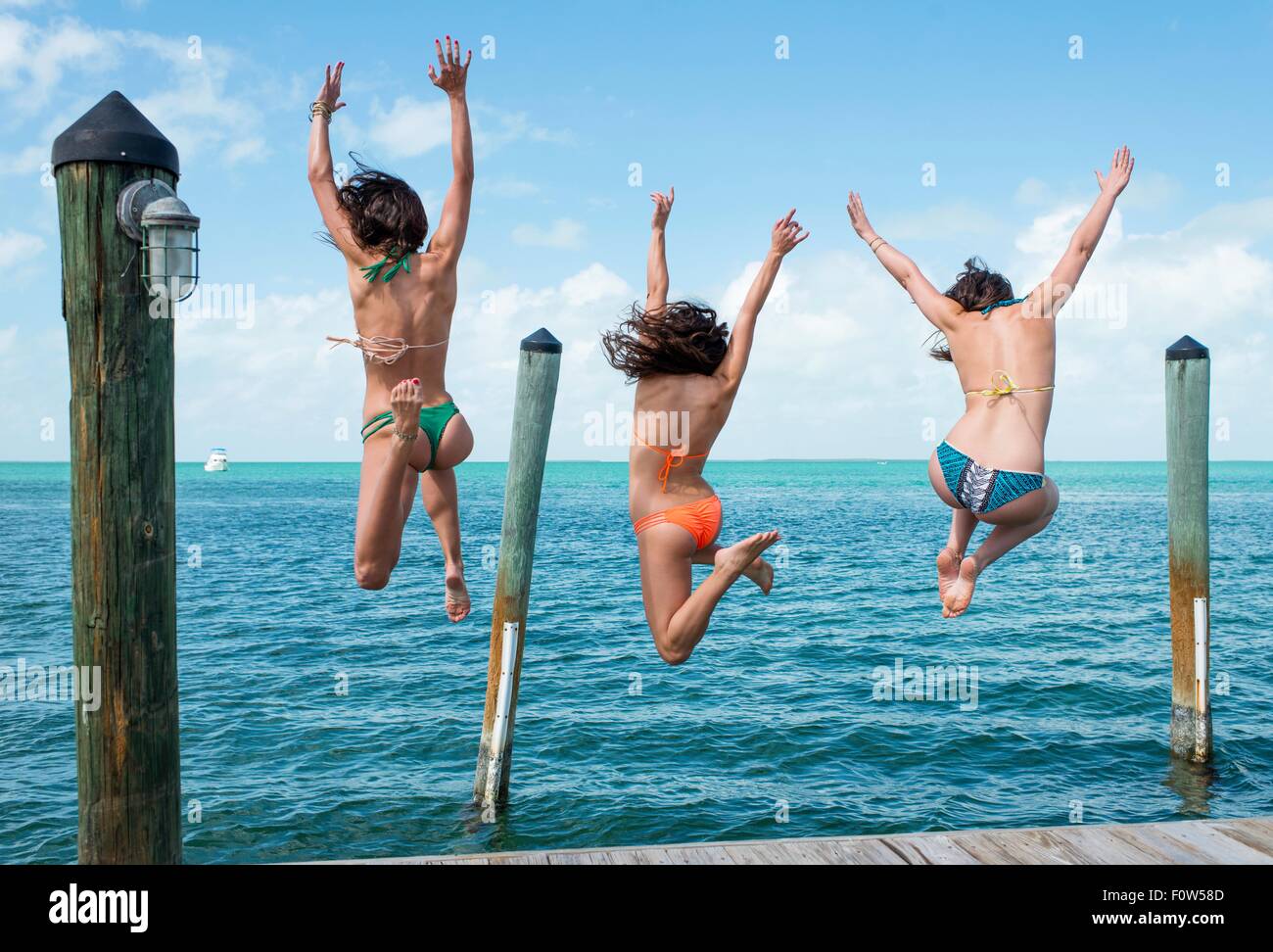 Vue arrière de trois jeunes femme sautant d'une mer pier, Islamorada, Florida, USA Banque D'Images