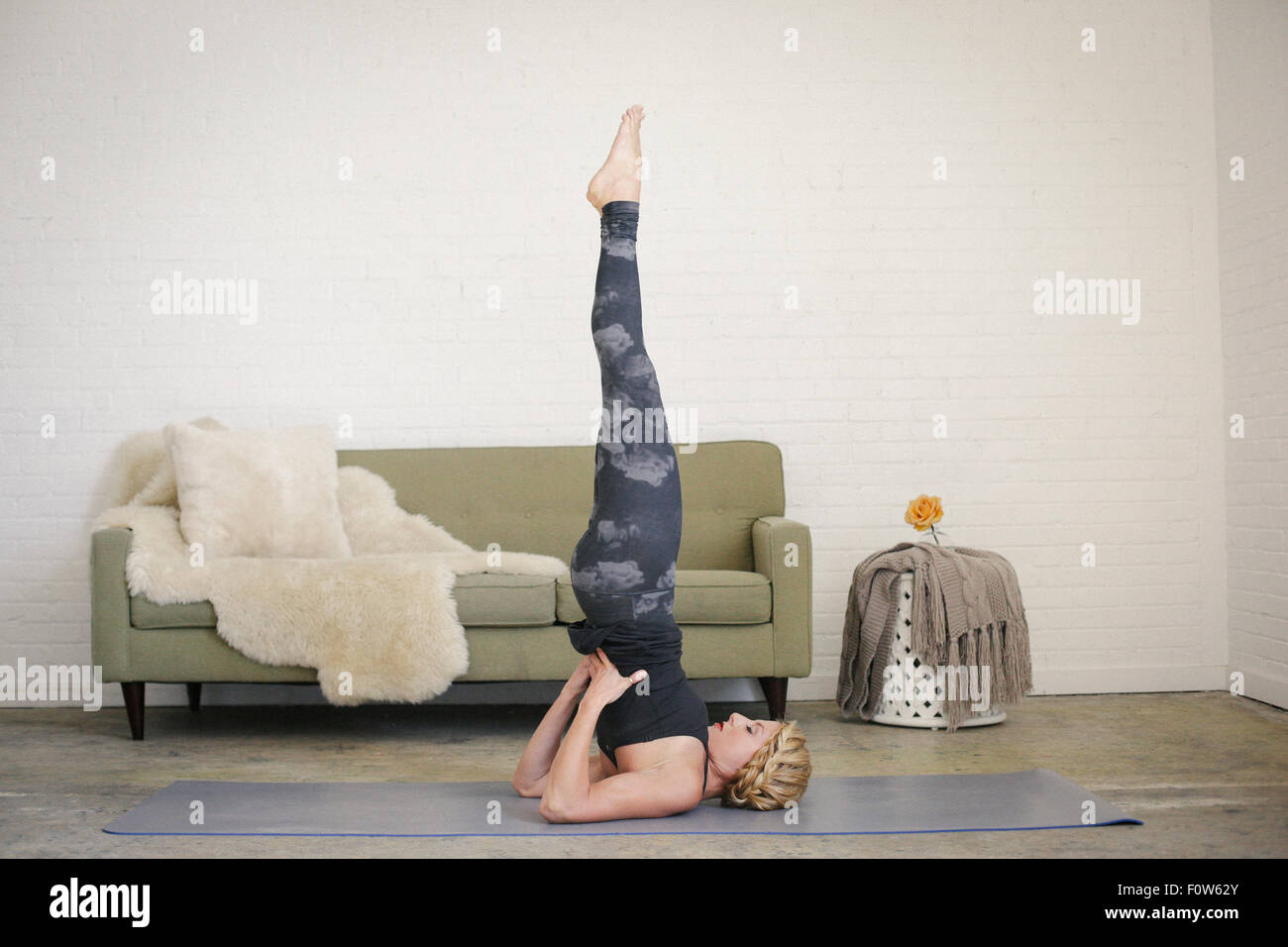 Une femme blonde dans un collant noir et des jambières, dans une posture sur sur un tapis de yoga dans une salle, faire du yoga. Banque D'Images