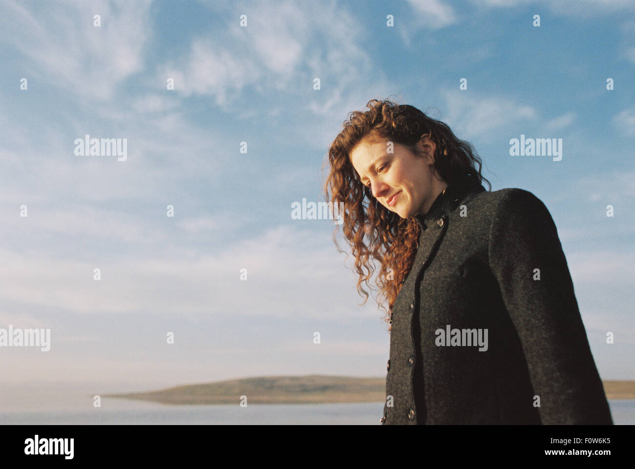 Femme avec Brown, de long cheveux bouclés et debout sur le bord d'un lac. Banque D'Images