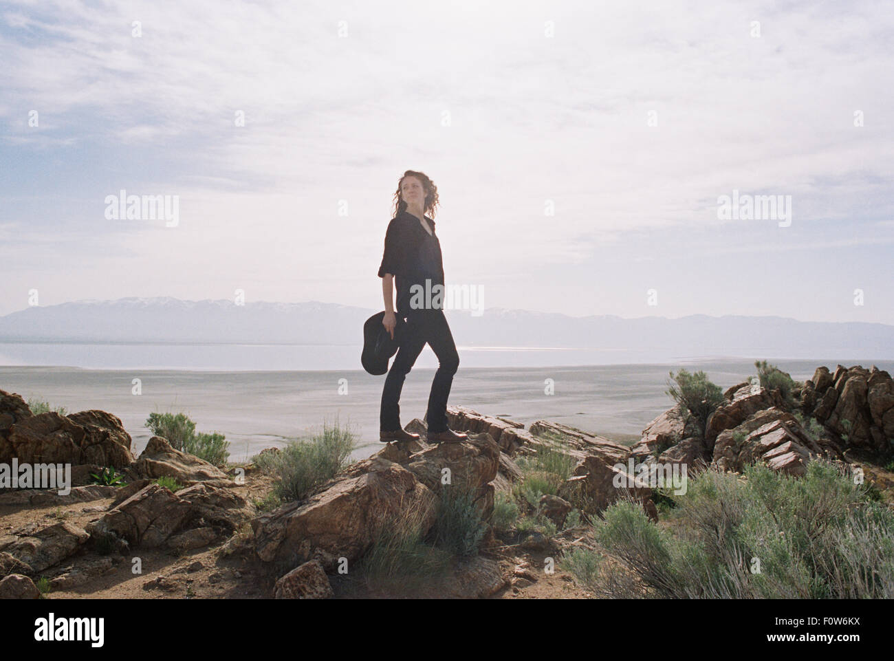Femme avec brown, long et frisés debout sur les rochers, un lac et les montagnes au loin. Banque D'Images