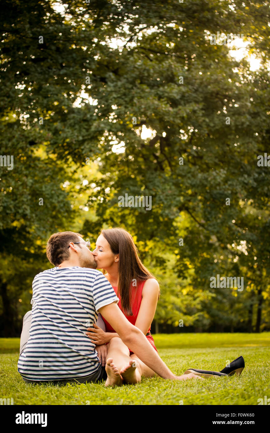 Young smiling couple assis et en l'embrassant sur l'herbe - femme nu-pieds avec des chaussures à côté d'elle Banque D'Images