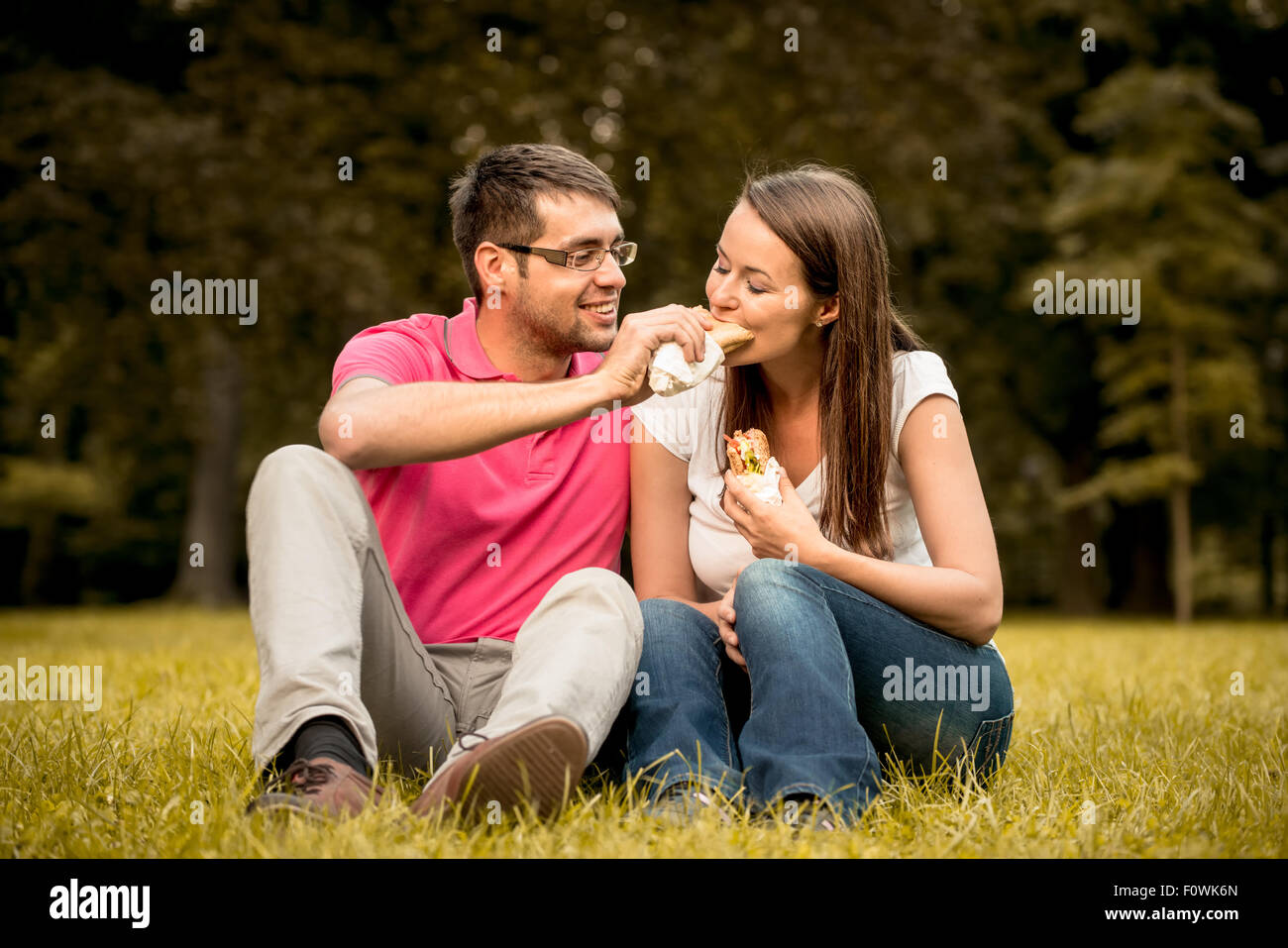 Couple eating sandwich en plein air et le partage de la nature Banque D'Images