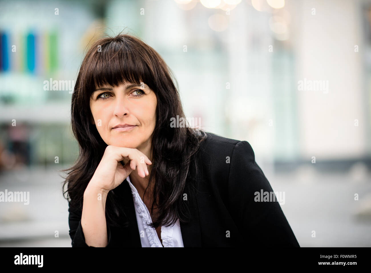 Portrait de senior business woman avec office building en arrière-plan, la main sous le menton Banque D'Images