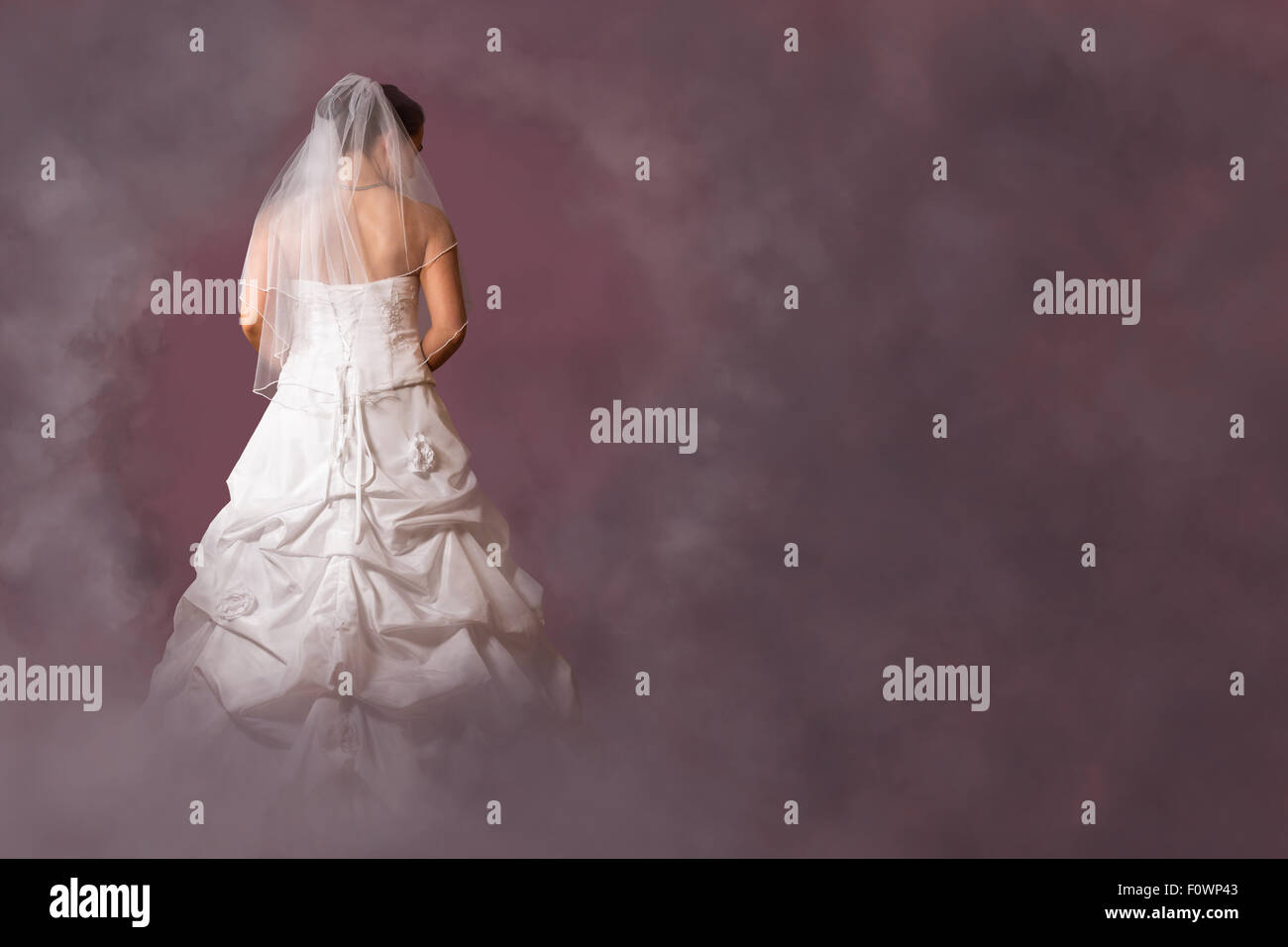 Jeune femme en robe de mariée dans un environnement nuageux rose Banque D'Images