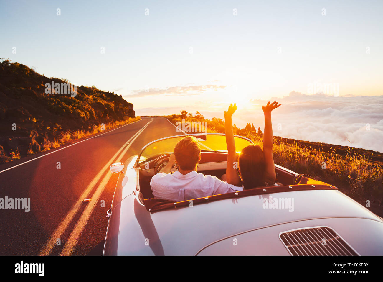 Couple heureux de la conduite sur route de campagne dans le coucher du soleil en voiture de sport Classic vintage Banque D'Images