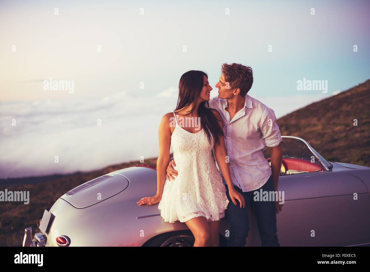 Jeune Beau couple romantique en admirant le coucher du Soleil avec Classic vintage Sports Car Banque D'Images