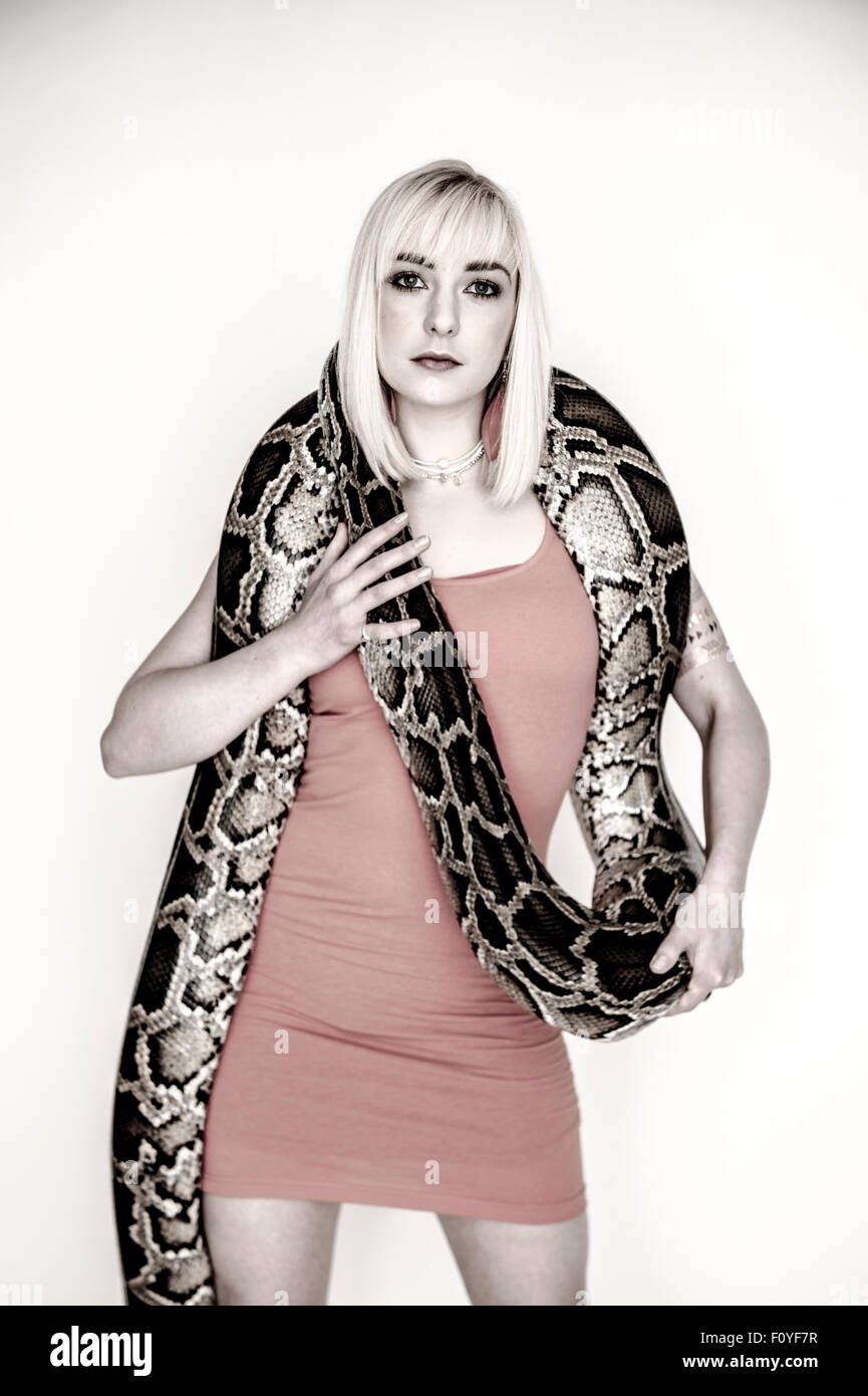 Une jeune femme fille femme personne portant une robe rouge posant debout  avec un serpent python drapé sur ses épaules , UK (ne souffre pas  d'ophiophobia - la peur des serpents Photo