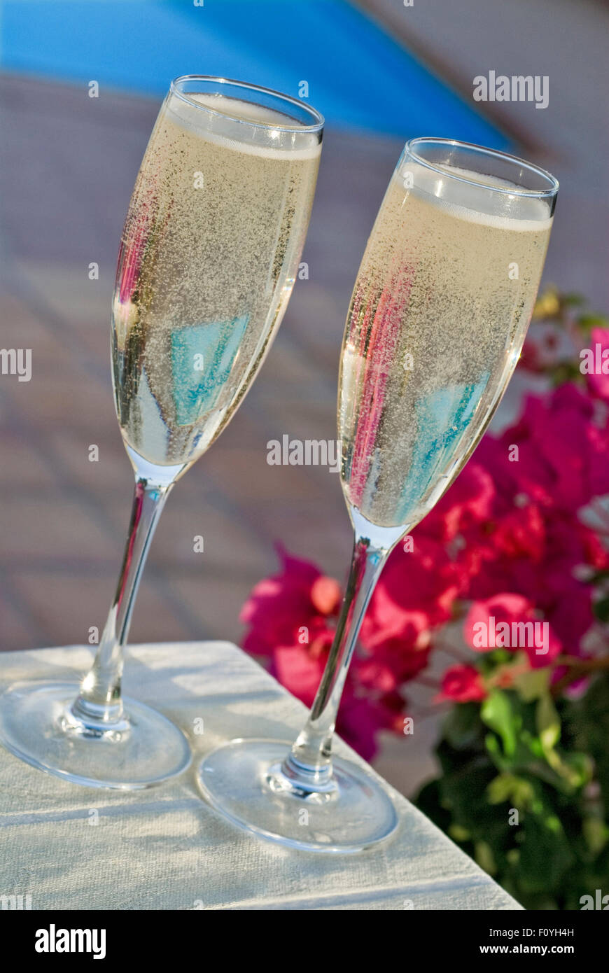 Champagne en plein air verres sur une terrasse ensoleillée avec bougainvilliers fleurs et piscine derrière le cadre de vacances exotiques de luxe Banque D'Images