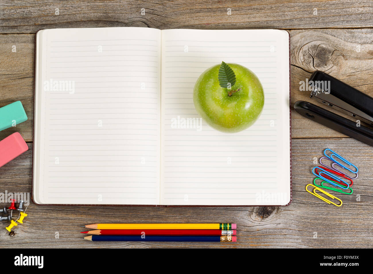 Vue de dessus, ouvrez le bloc-notes de pomme verte entourée de fournitures en bois rustique. Banque D'Images