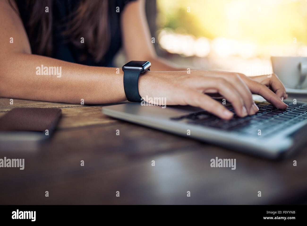 Mains de femme portant smartwatch sur le clavier de son ordinateur portable. Les femmes travaillant sur ordinateur portable dans un café. Banque D'Images