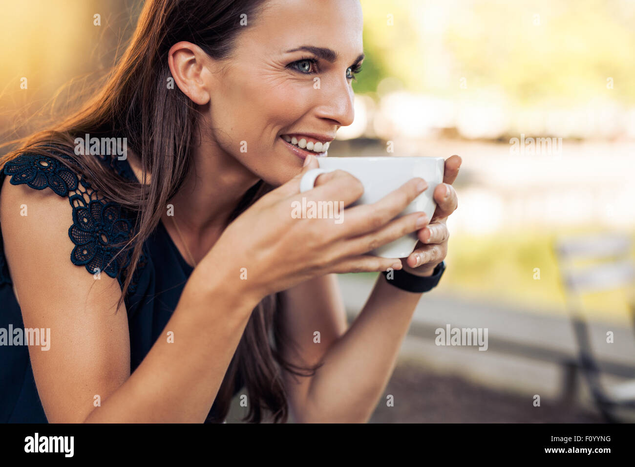 Jeune femme tenant une tasse de café et à la voiture en souriant. Les femmes de race blanche de boire du café au café. Banque D'Images