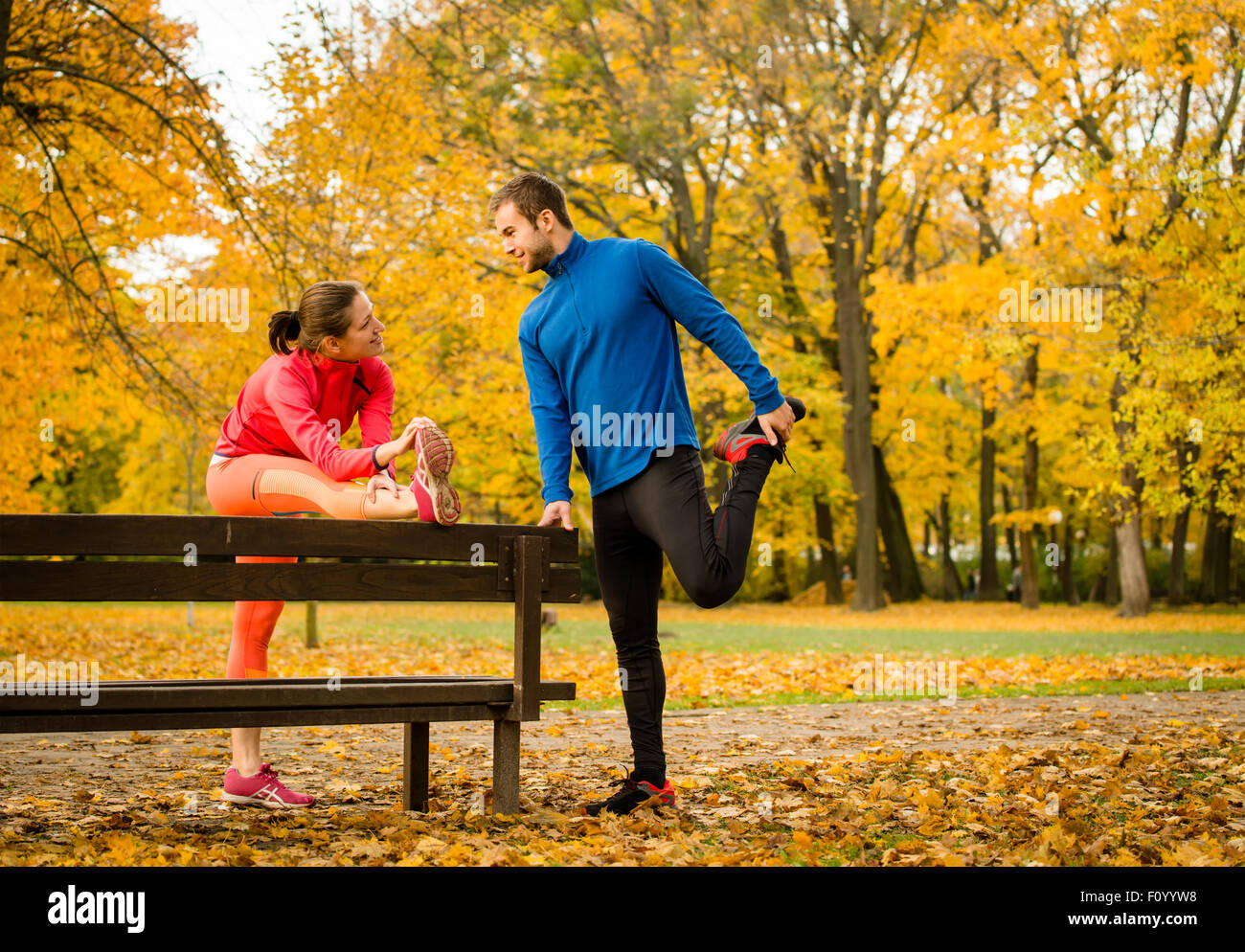 Jeune couple stretching muscles sur banc avant de jogging en automne nature Banque D'Images