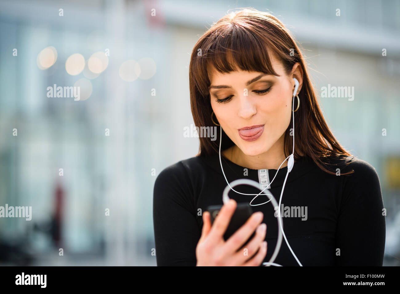 Young woman sticking out tongue tout en faisant appel vidéo dans Street Banque D'Images