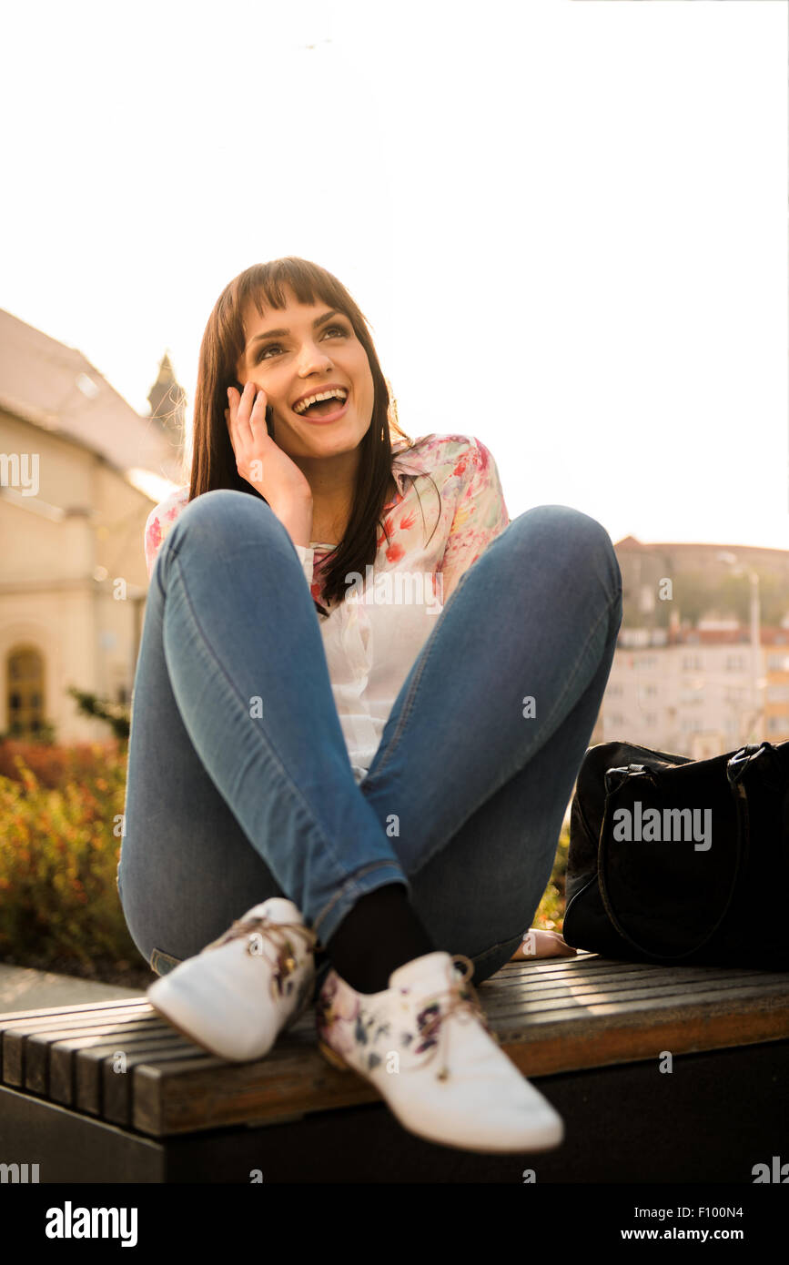 Photo authentique de jeunes femme appelant téléphone - sitting on bench in street Banque D'Images