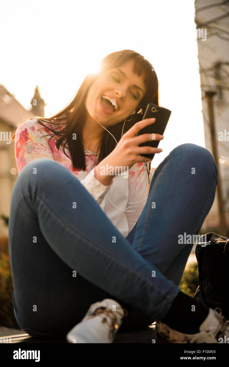 Jeune femme à l'écoute de la musique à partir de son téléphone et le chant en street avec en arrière-plan Banque D'Images