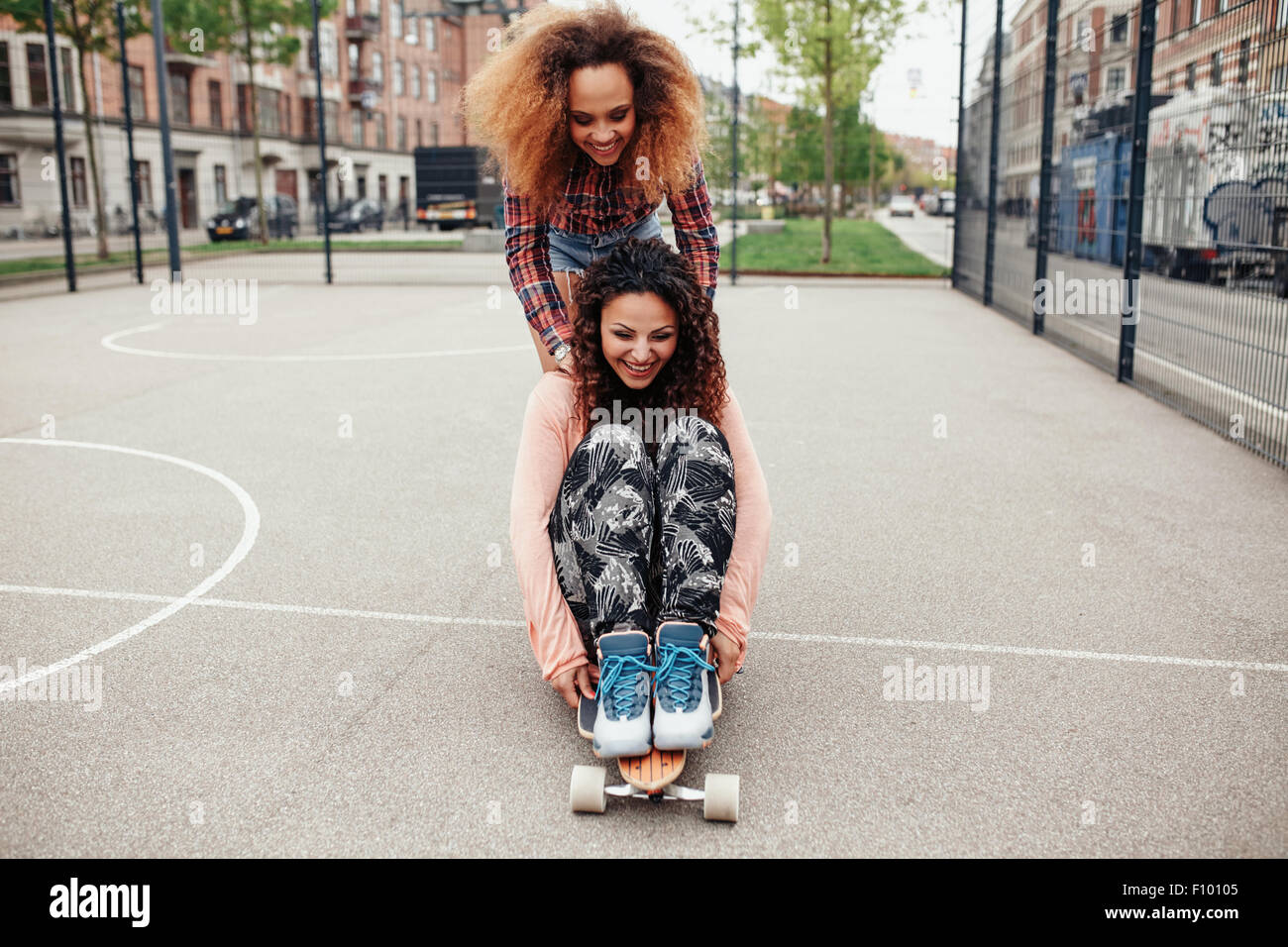 Femme poussant son ami sur longboard. Les filles en patinage de Hipster un  terrain de basket dans la ville Photo Stock - Alamy