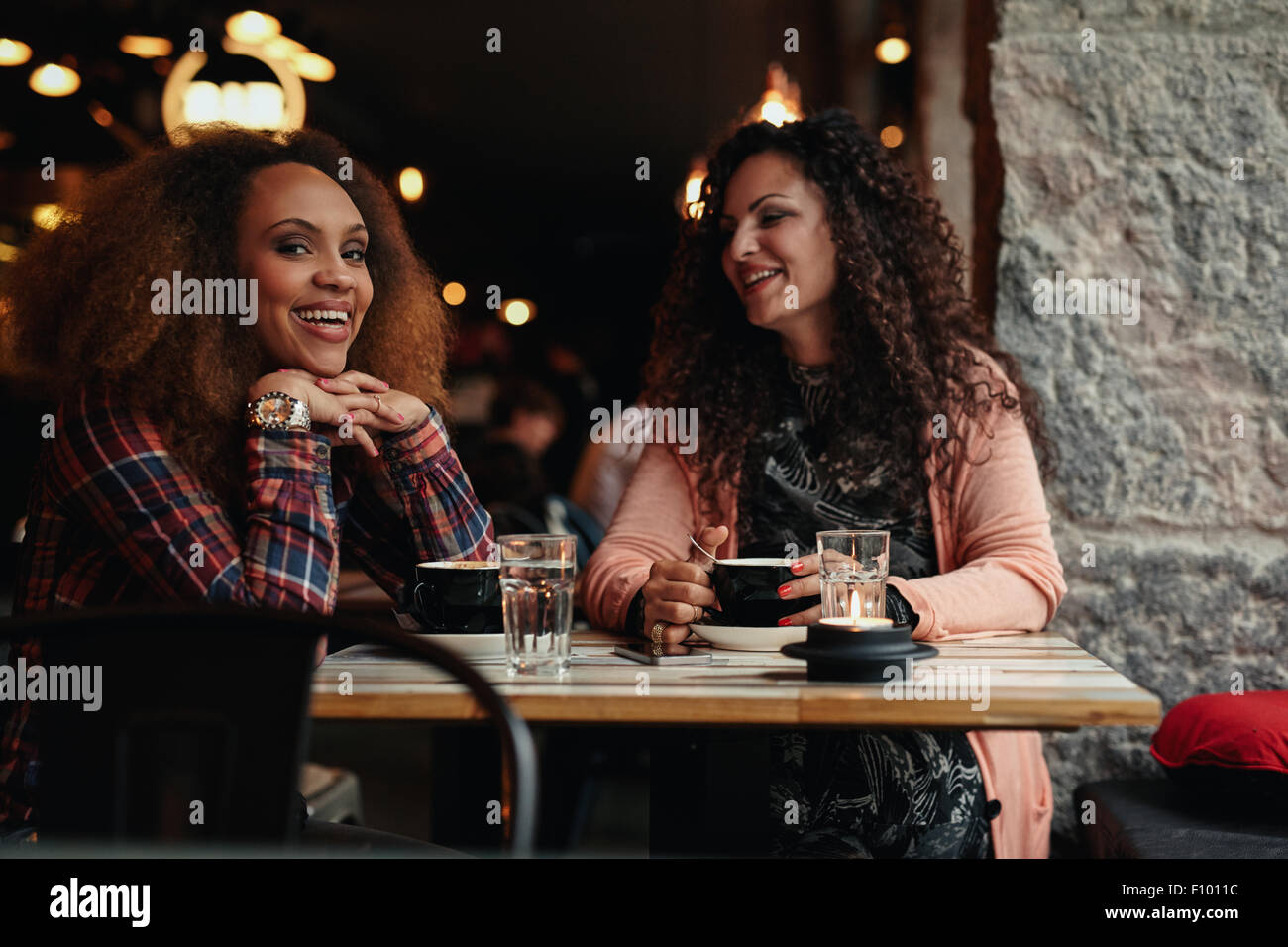 Deux femmes assises dans un restaurant en souriant. Jeunes amis dans un café, avec un appareil photo en souriant. Banque D'Images