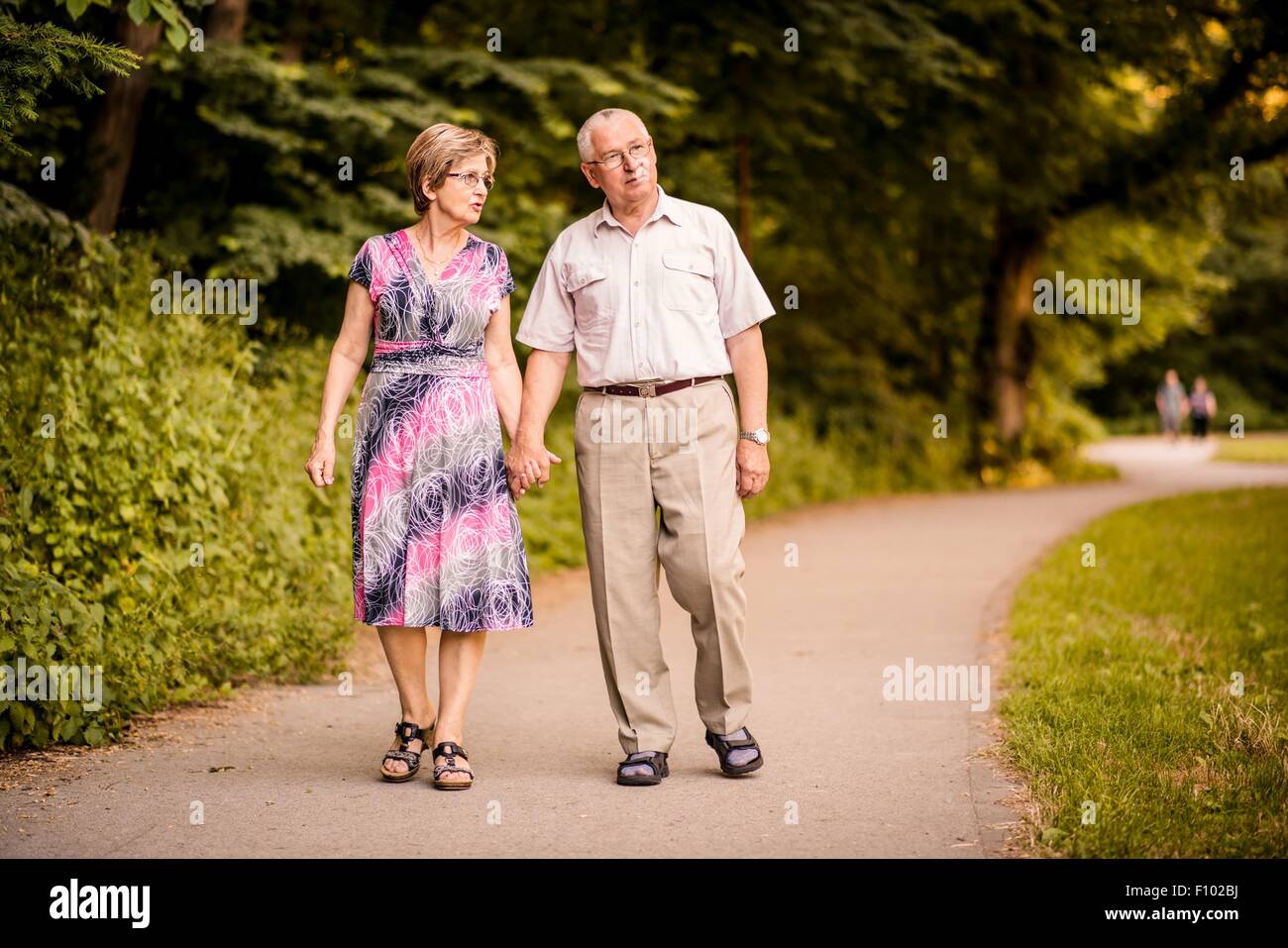 Happy senior couple walking holding hands in forest park Banque D'Images