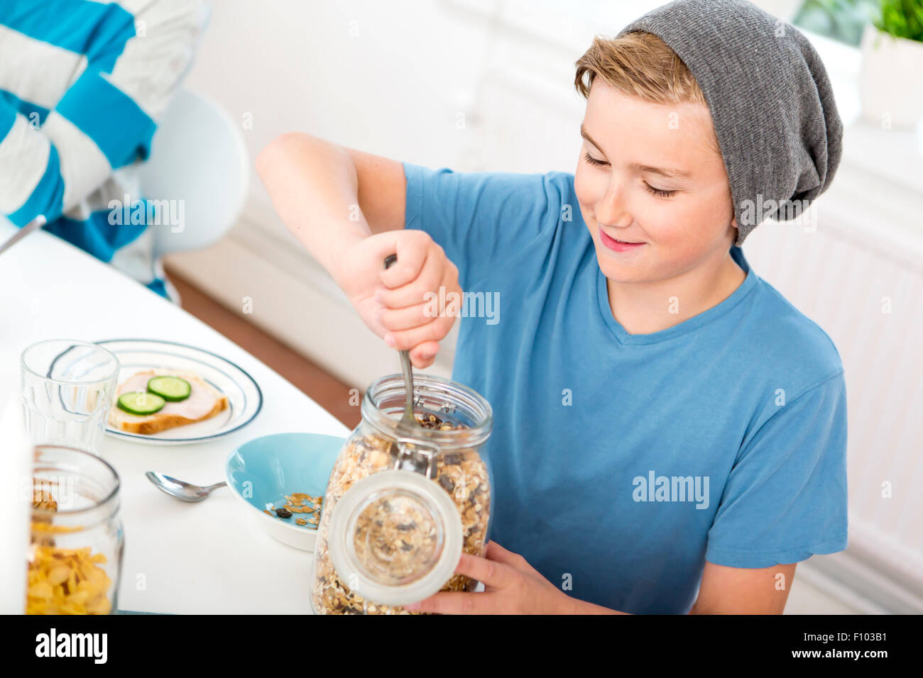 Teenage boy servant de céréales une bouteille à la table du petit déjeuner. Banque D'Images