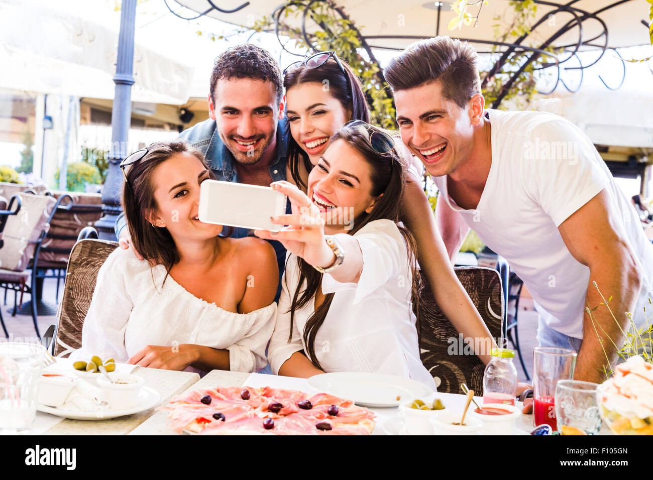 Groupe de jeunes gens assis dans un beau restaurant et prendre un en souriant selfies Banque D'Images