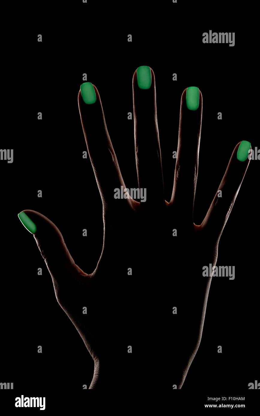 La main féminine silhouette sur fond noir avec contour vert d'éclairage et de design sur ongles luminescent Banque D'Images