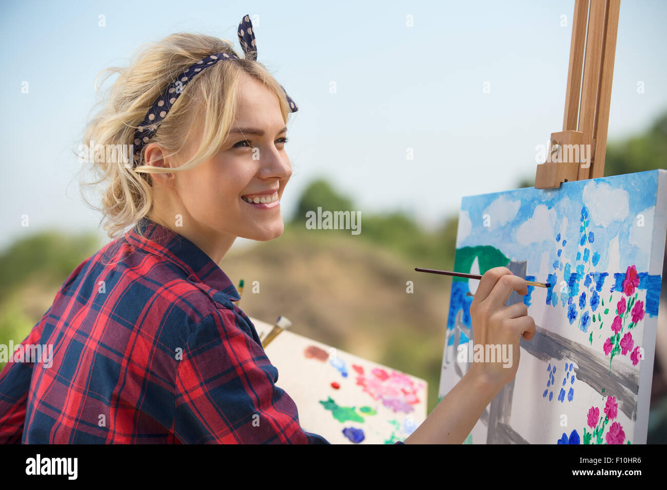 Belle blonde femme artiste peint une image colorée. Banque D'Images