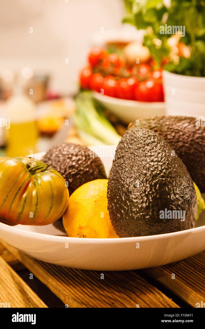 Bol de fruits sur le comptoir de la cuisine, contenant les avocats, les citrons et les tomates du patrimoine. Banque D'Images