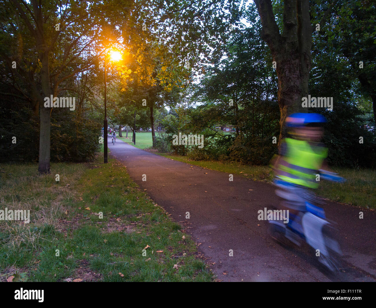 Les cycles d'un enfant son vélo dans un parc de Londres de nuit avec un éclairage lumineux au crépuscule à la fin de l'été Banque D'Images